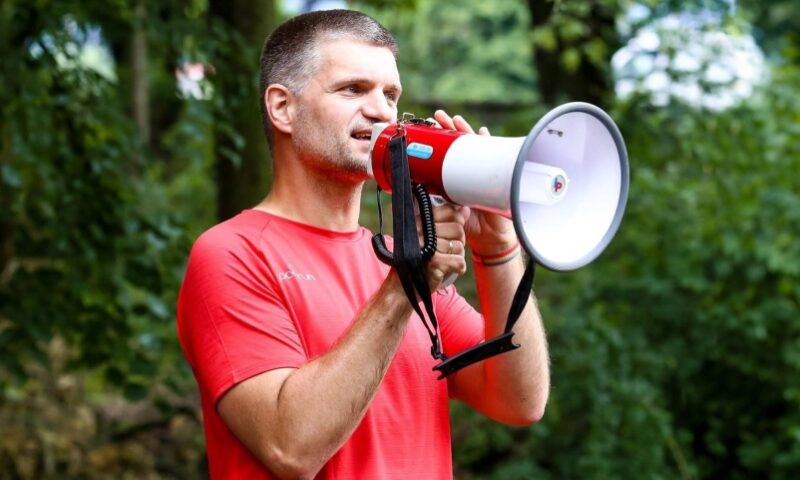 Mężczyzna w czerwonej koszulce, mówiący przez megafon